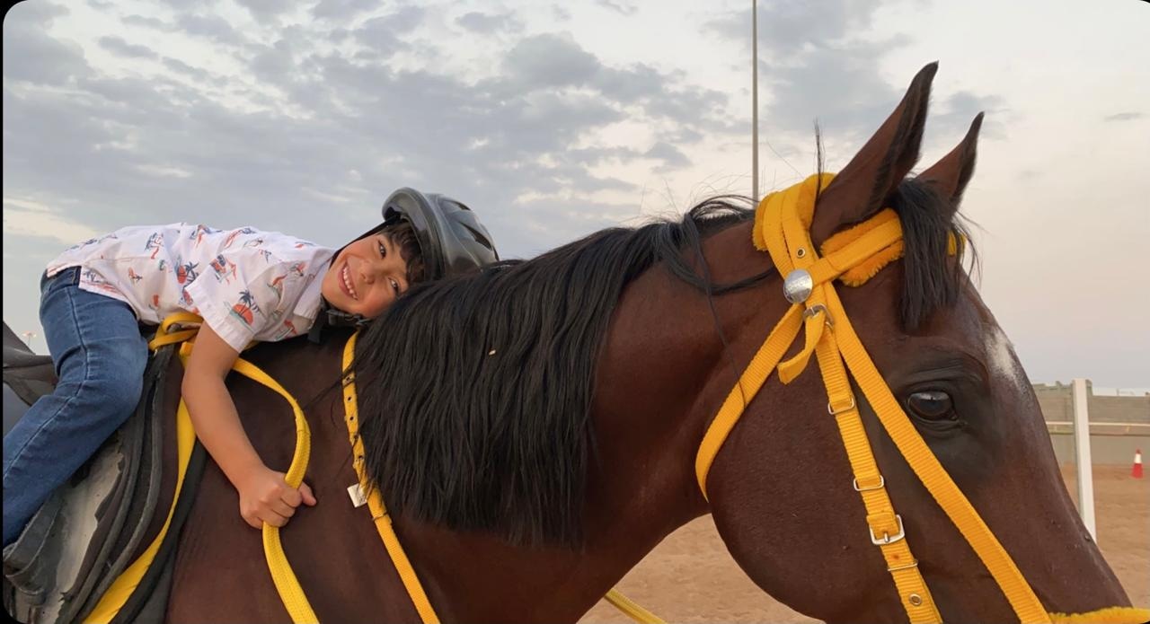 A helmeted boy leaning affectionately on his horse at Albarraq